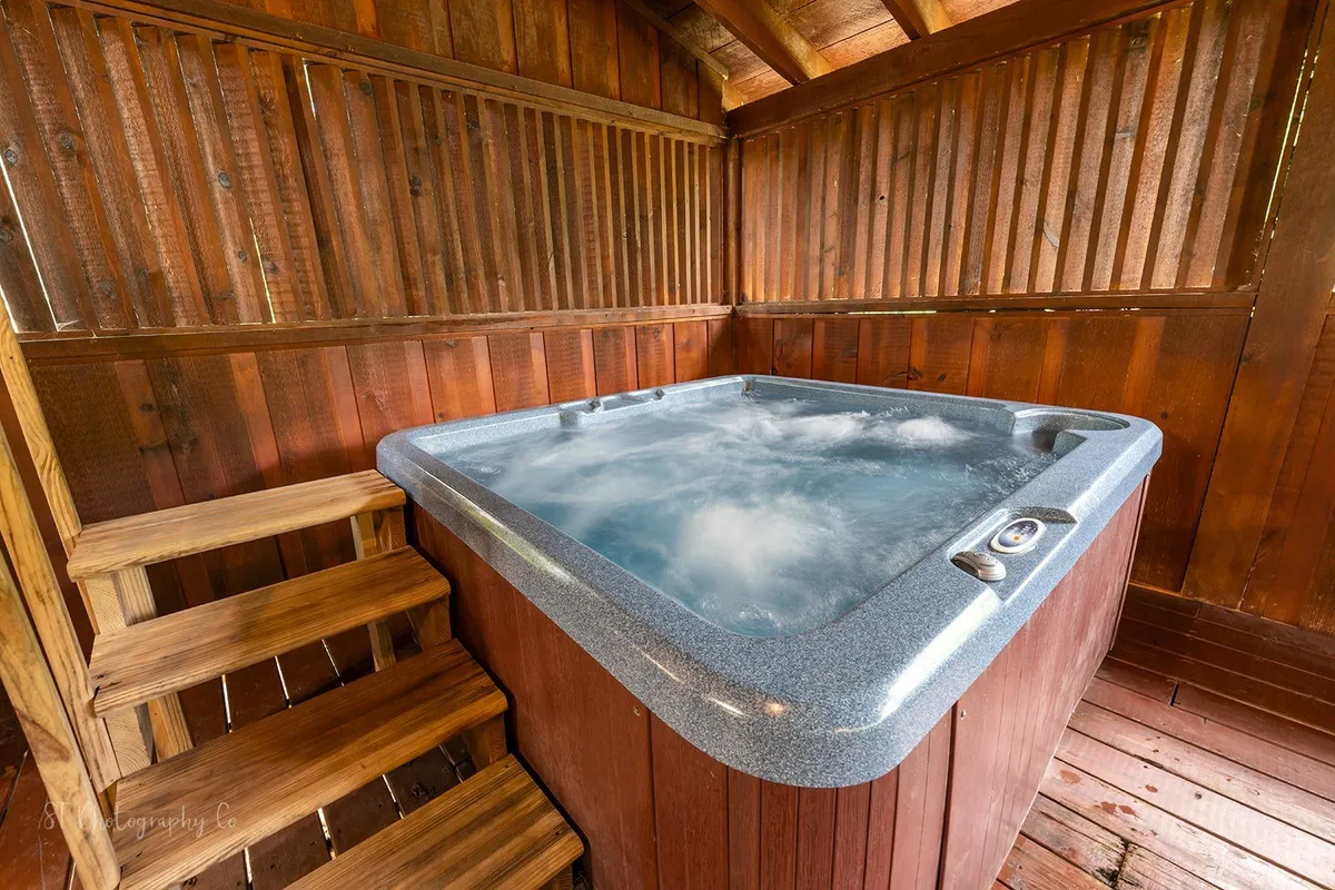 A tranquil interior scene with a bubbling hot tub set against wood paneling and wooden steps. The setup suggests relaxation, with the hot tub presenting a perfect retreat after a day in the mountains.