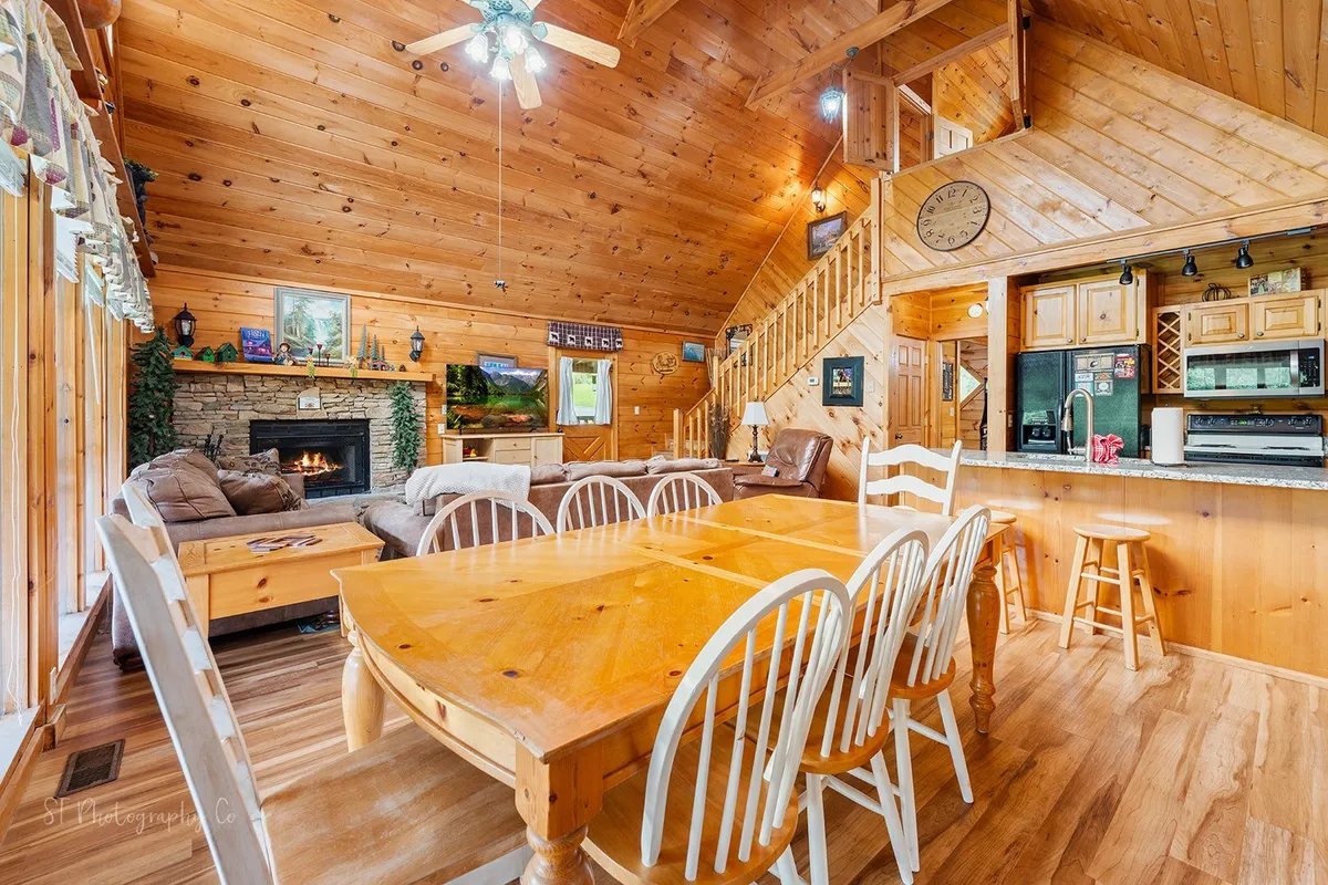 A warm, inviting shot that captures the dining table, fireplace, sofa, staircase, and kitchen area. The layout emphasizes communal meals, family games, and relaxation after a day outdoors, all within sight of the kitchen for easy conversation and flow.